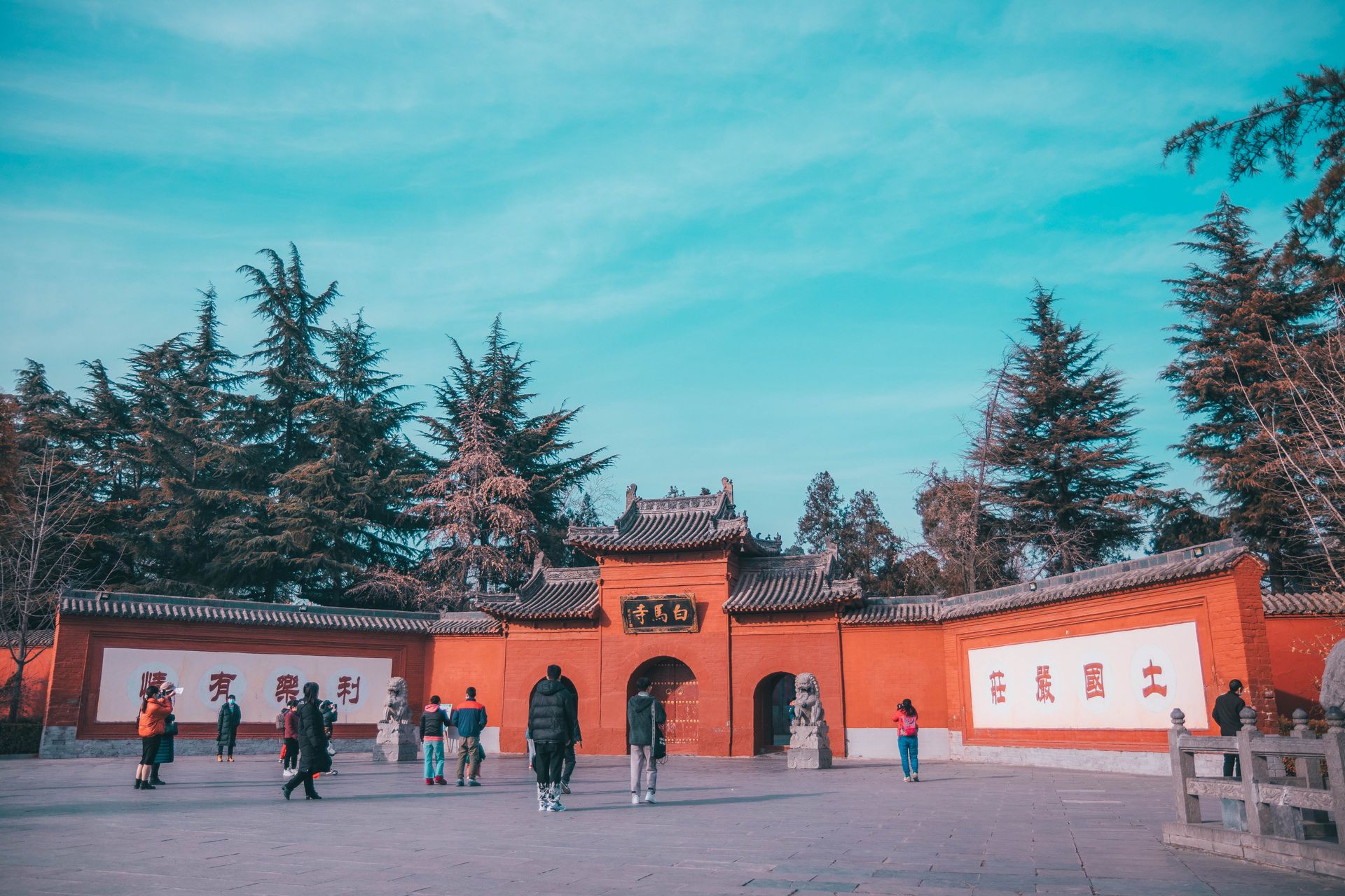 Tourists exploring an ancient Chinese temple entrance surrounded by lush trees.