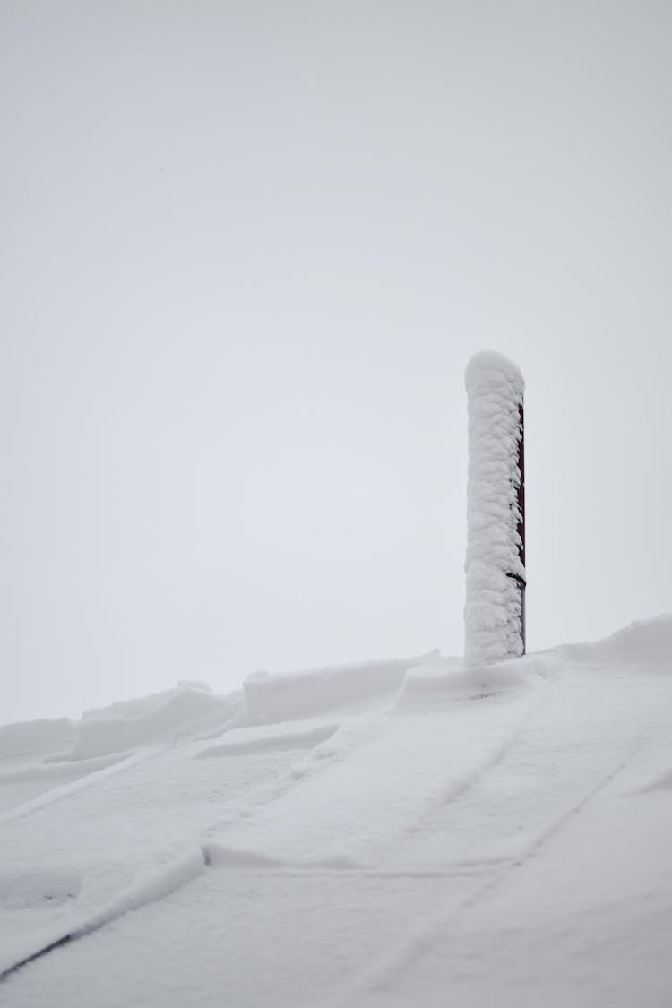 A Snow Covered Roof And Chimney Under The White Sky