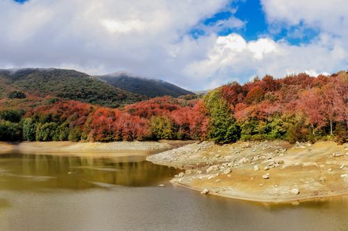 Free Scenic view of a lake surrounded by colorful autumn foliage and distant hills. Stock Photo