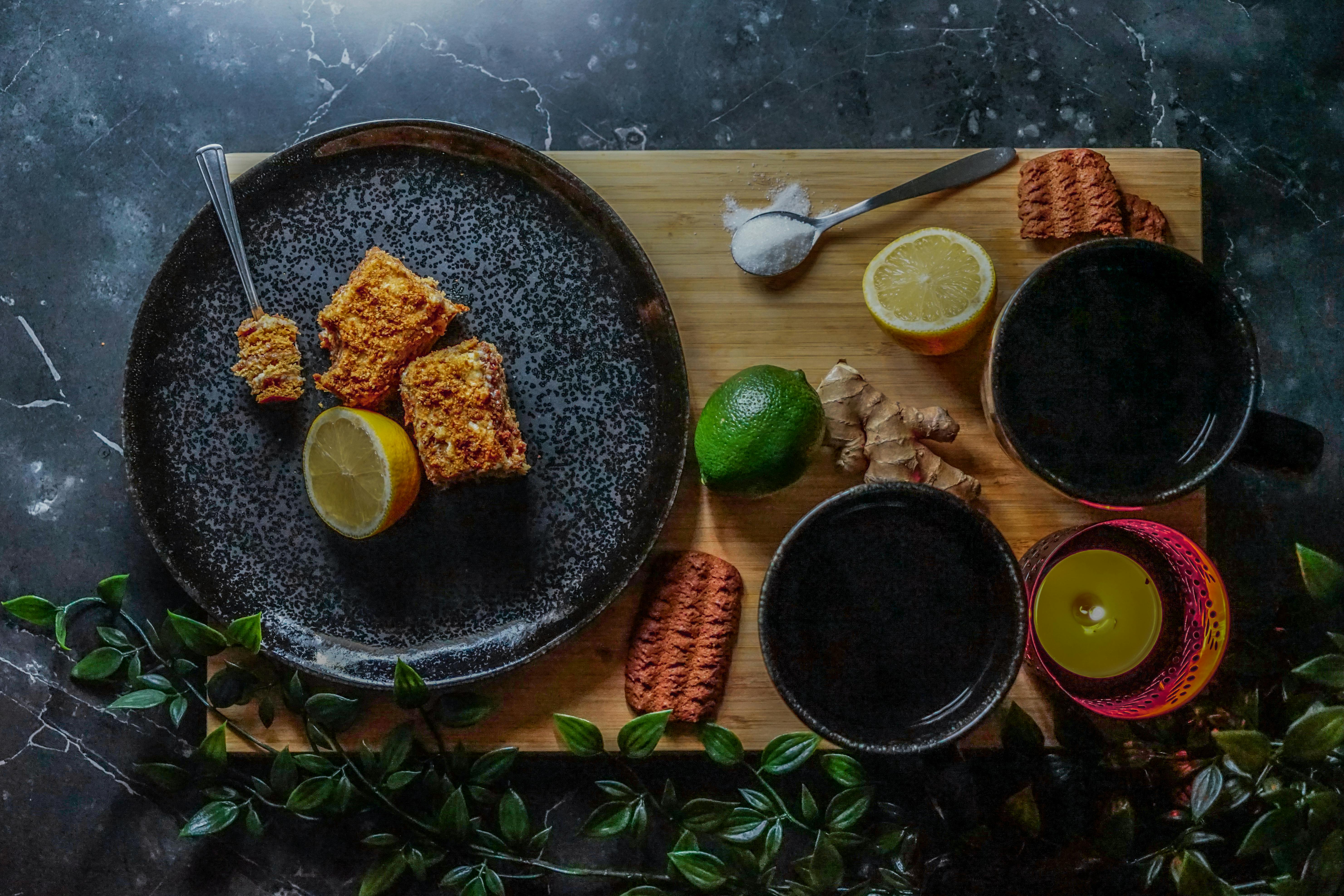 Flat lay of a gourmet dessert setup with lemon, lime, ginger, and cookies on a marble background.