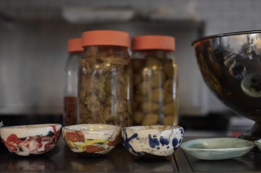 Artistic close-up of colorful ceramic bowls and jars of fermented food on a kitchen counter.