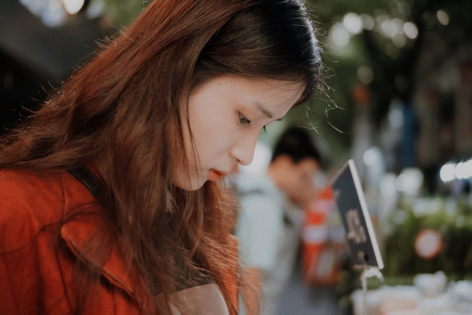Close-up profile of a young woman in a red jacket with a blurred outdoor background.