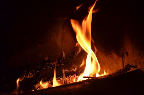 Burning firewood with bright orange flames in fireplace in dark room at night
