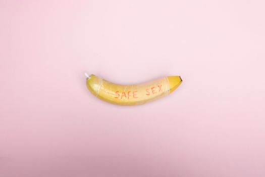 Still life image of a banana wrapped in a condom with 'safe sex' text on a pink background.