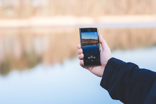 Free Man taking photo of a lake with mobile phone Stock Photo