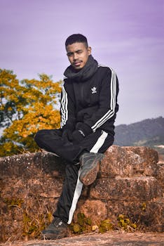 Asian man in black sportswear sitting on a rock with scenic autumn background.