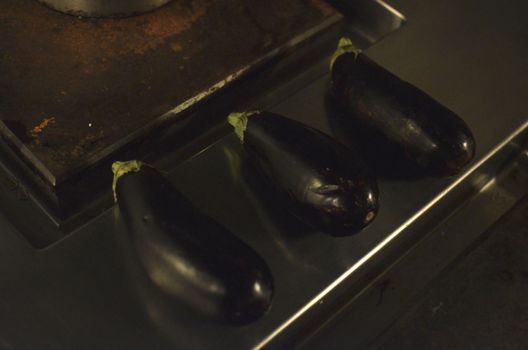 Top view of three fresh eggplants placed on a stainless steel kitchen counter, showcasing a rustic setting.