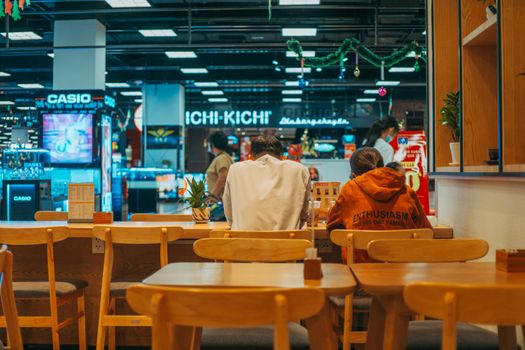 People dining in a contemporary restaurant inside a bustling mall with vibrant lights.