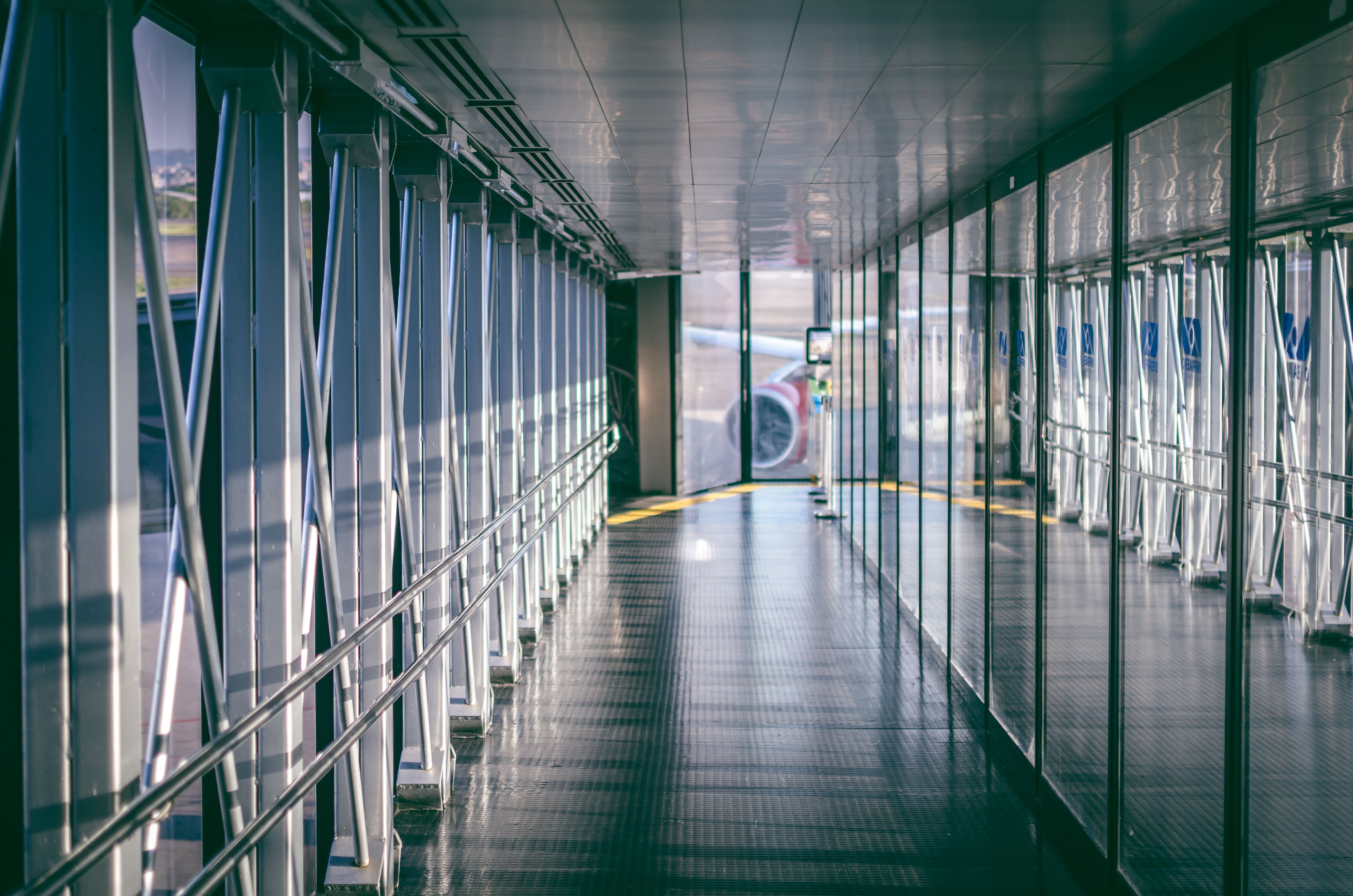 Empty airport boarding bridge corridor with glass walls and an airplane visible outside.