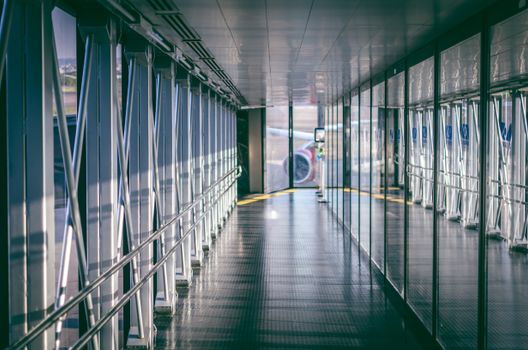 Sunlit airport jet bridge with reflections and aircraft visible outside, RS, Brazil airport.