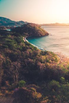 From above picturesque view of trees on mount against sea under light sky at sundown
