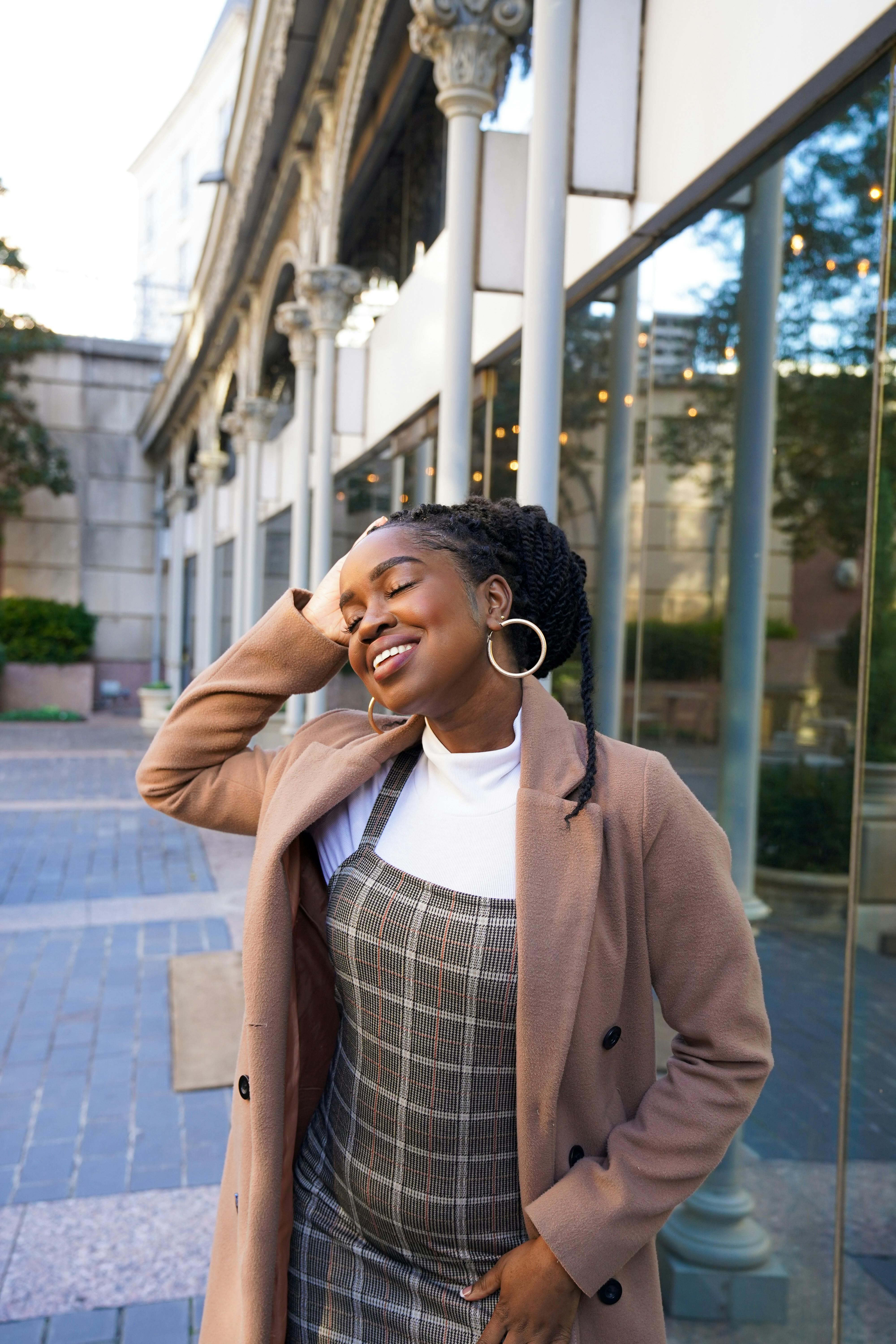 African American woman posing outdoors, smiling with eyes closed in stylish winter attire.