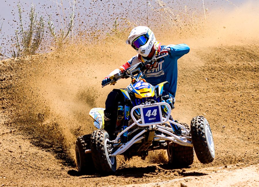 An ATV rider in full gear maneuvers through a dirt track, showcasing skill and motion.