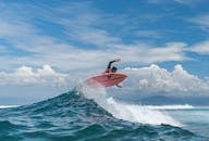 African American sportsman on surfboard over splashing sea water practicing surfing under blue cloudy sky