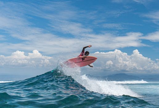 African American sportsman on surfboard over splashing sea water practicing surfing under blue cloudy sky