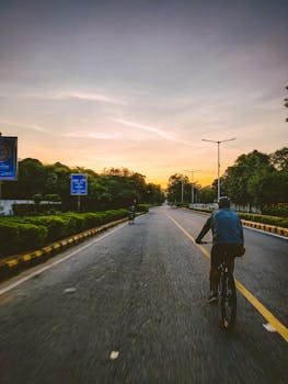 A cyclist pedals along a New Delhi road at sunset, capturing the vibrant city atmosphere.