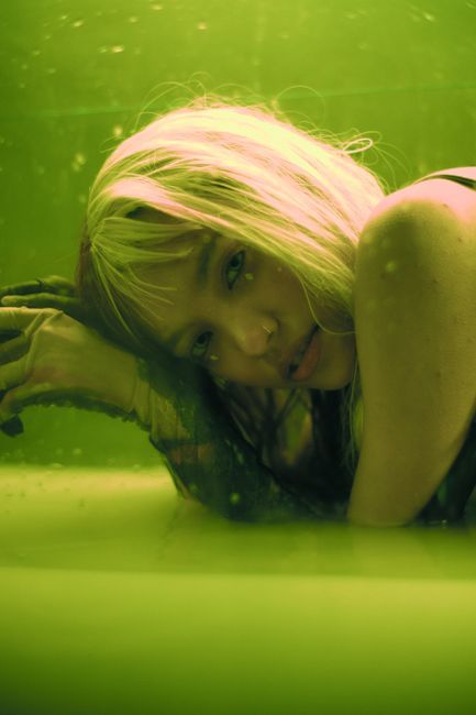 Conceptual photo of a woman with blonde hair submerged in water under green lighting, evoking emotion.