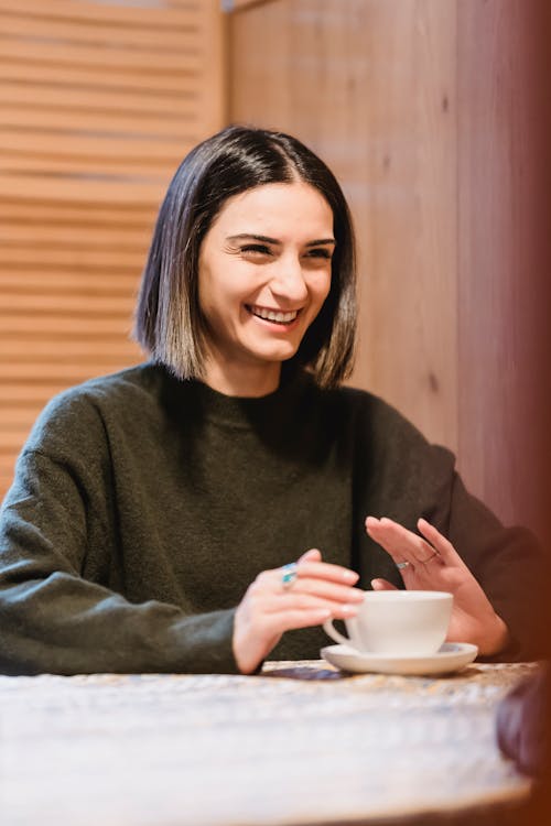 Cheerful woman with cup of coffee smiling at table