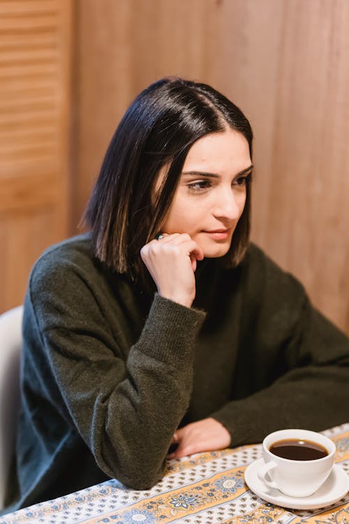 From above of young female touching chin at table with cup of coffee in cafe