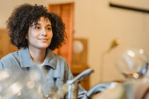 Content young female with dark Afro hair smiling and looking away on blurred background