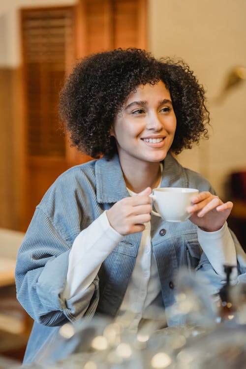 Young cheerful woman with Afro hairstyle drinking coffee