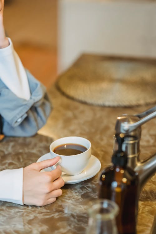 Free Crop anonymous female with cup of tasty aromatic coffee at table on blurred background of kitchen Stock Photo