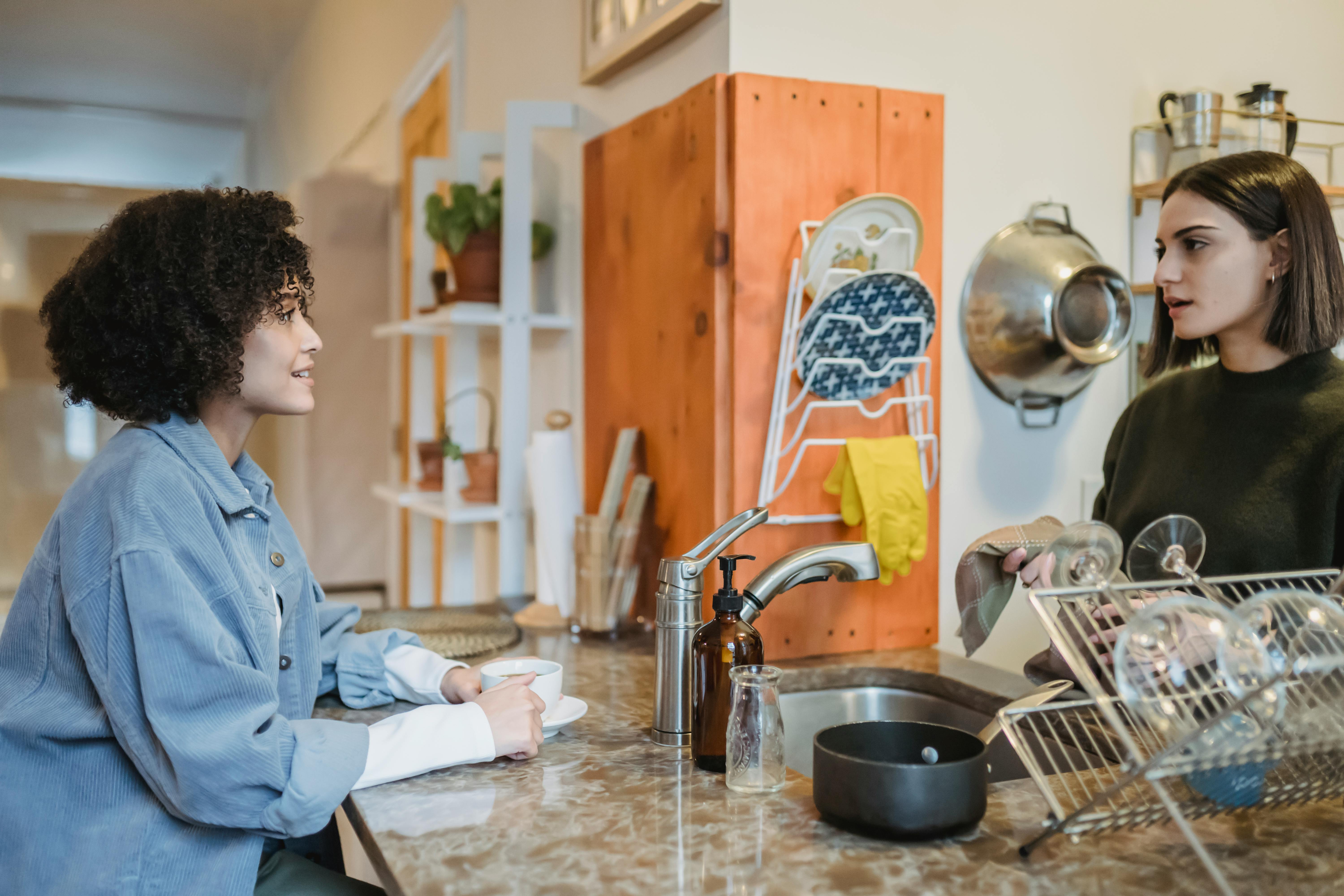 young women chatting in kitchen while drinking coffee and cleaning