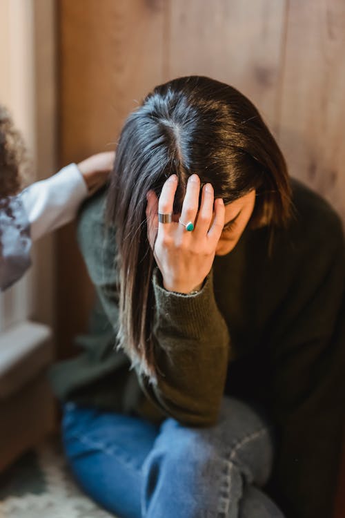 From above of young exhausted sad female in sorrow with supporting crop anonymous friend