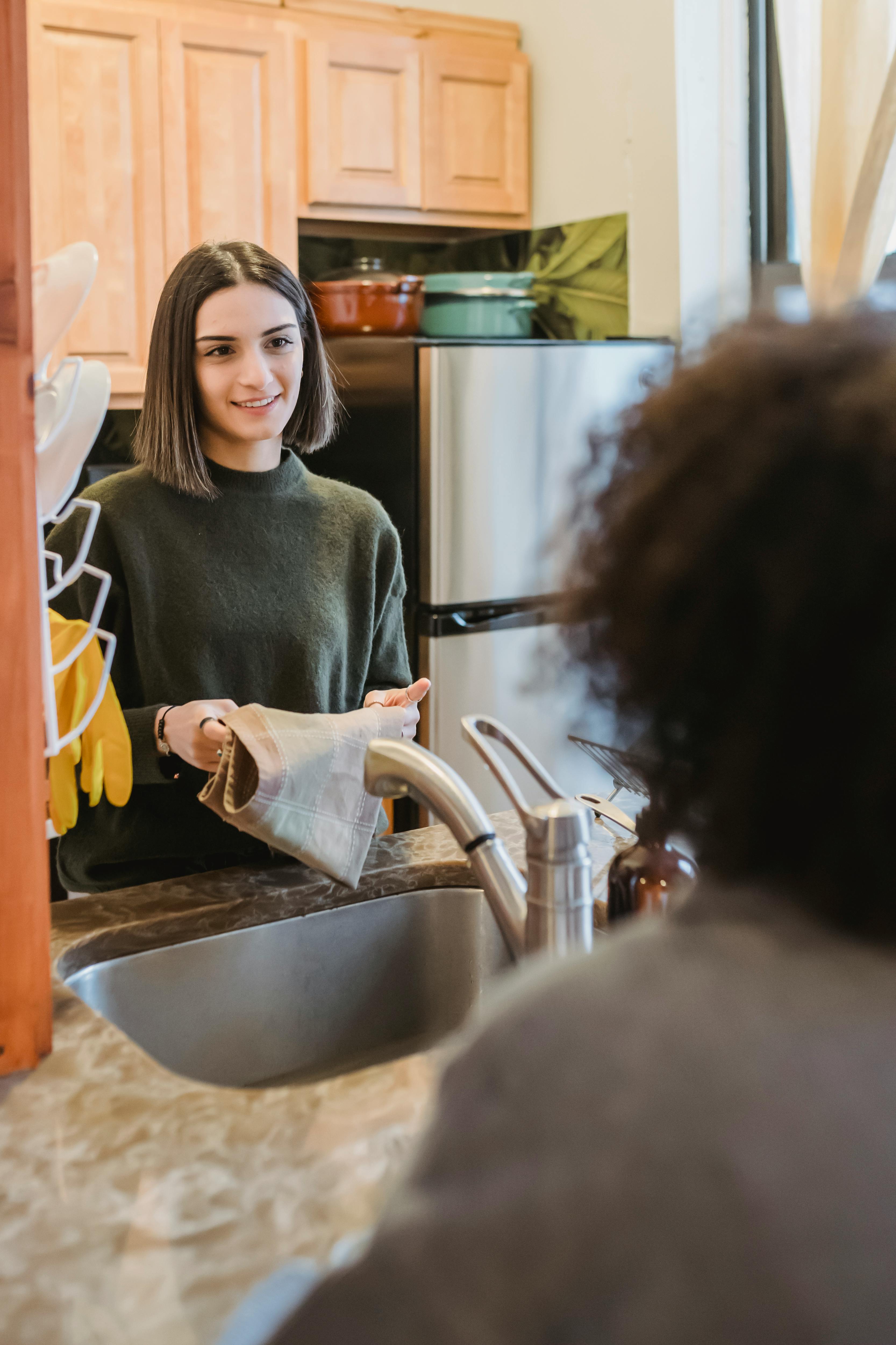 woman speaking with glad friend cleaning kitchen