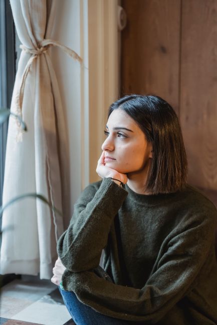 Young female with dark short hair looking away while leaning on hand at home