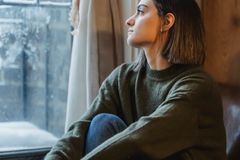 Side view of young female sitting in solitude and thoughtfully looking in window