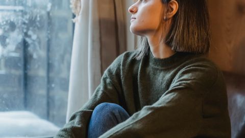 Side view of young female sitting in solitude and thoughtfully looking in window