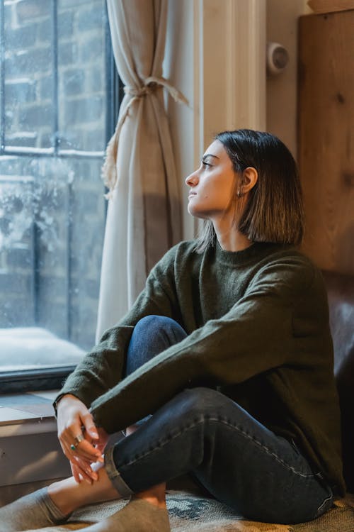Free Dreamy woman with crossed legs sitting near window Stock Photo