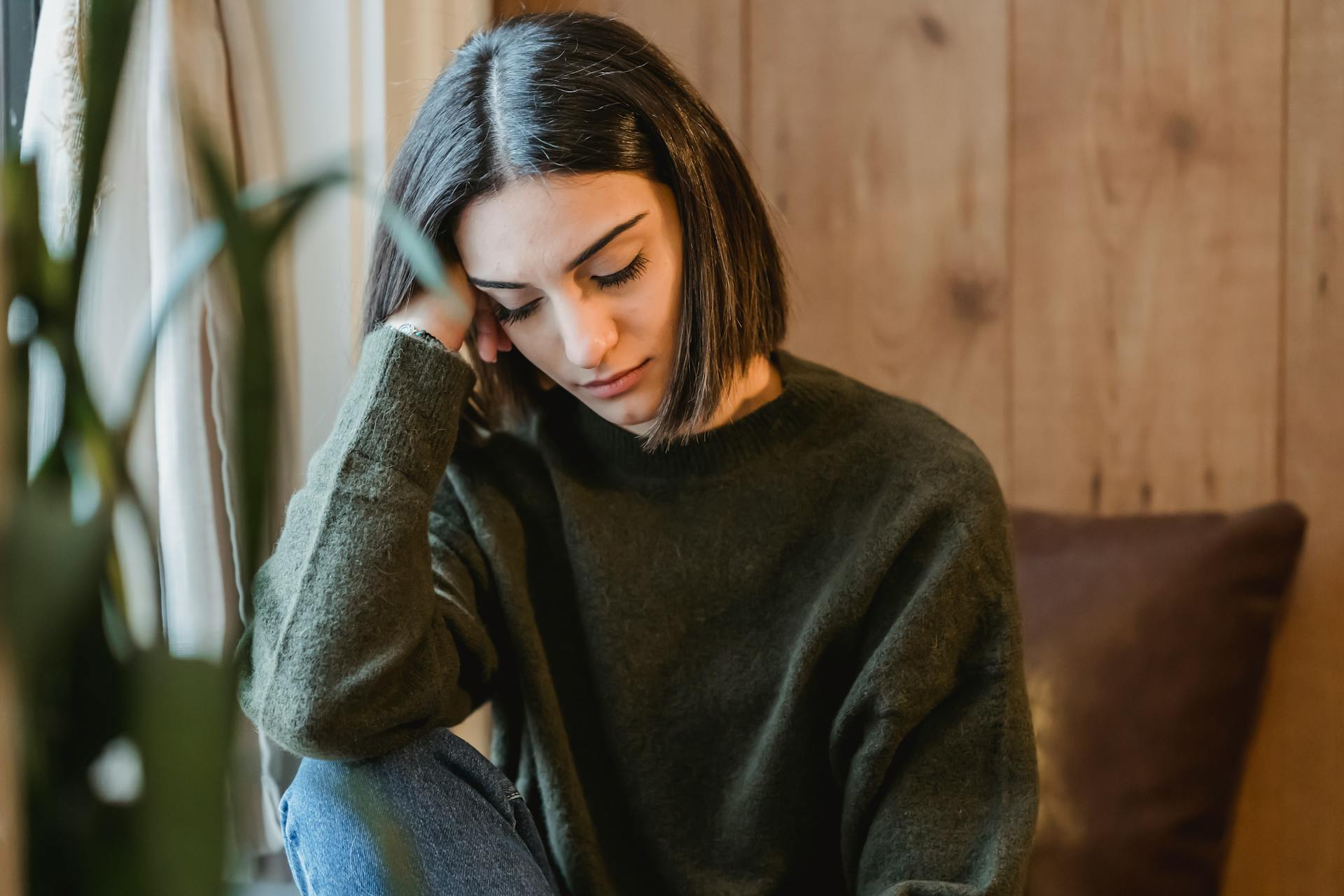 Tired female with closed eyes leaning on hand while having break and nap near window