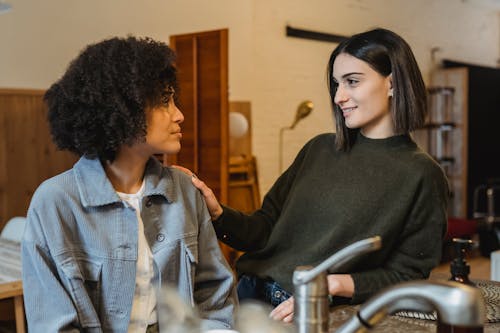 Positive female stroking shoulder of upset African American female friend with Afro hairdo and looking at each other