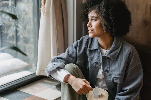 Free High angle of upset African American female suffering from loss and misfortune sitting on windowsill and looking away Stock Photo