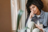 Sad African American female with tissue sitting on windowsill and crying while suffering from sorrow