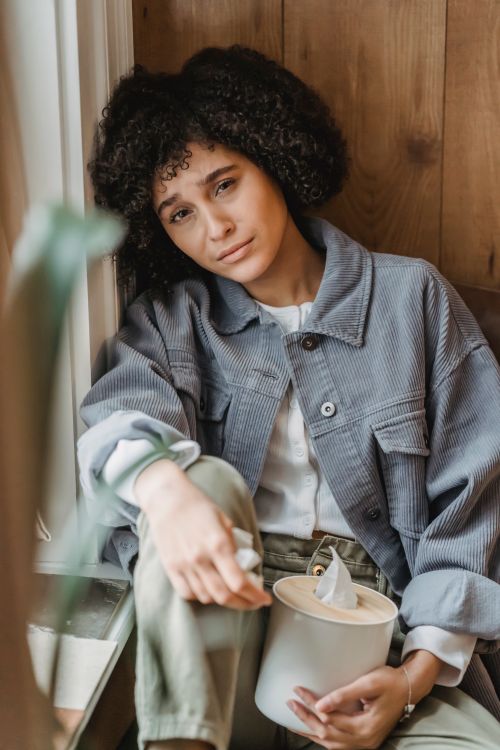 Free High angle of unhappy African American female with box of tissues sitting on windowsill and looking at camera Stock Photo