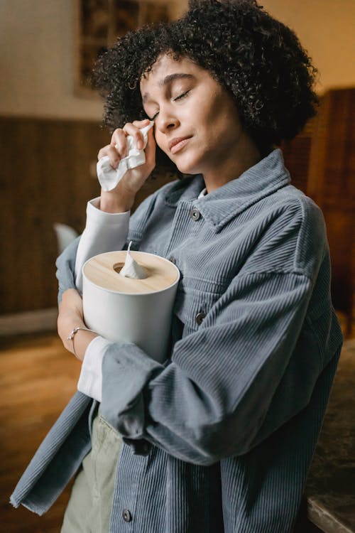 Side view of sad young African American female with curly hair in casual clothes crying and wiping tears with tissues