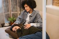 Depressed young ethnic lady in casual clothes crying while lying on knees of African American female best friend at home