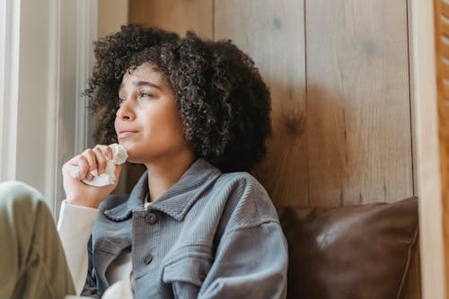 Thoughtful young ethnic lady crying near window at home