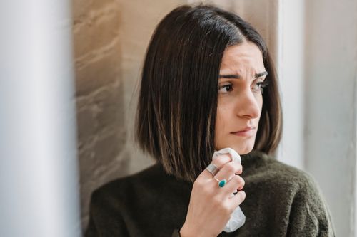 Free Sad young ethnic female millennial with dark hair standing near brick wall with tissue in hand and looking away thoughtfully Stock Photo