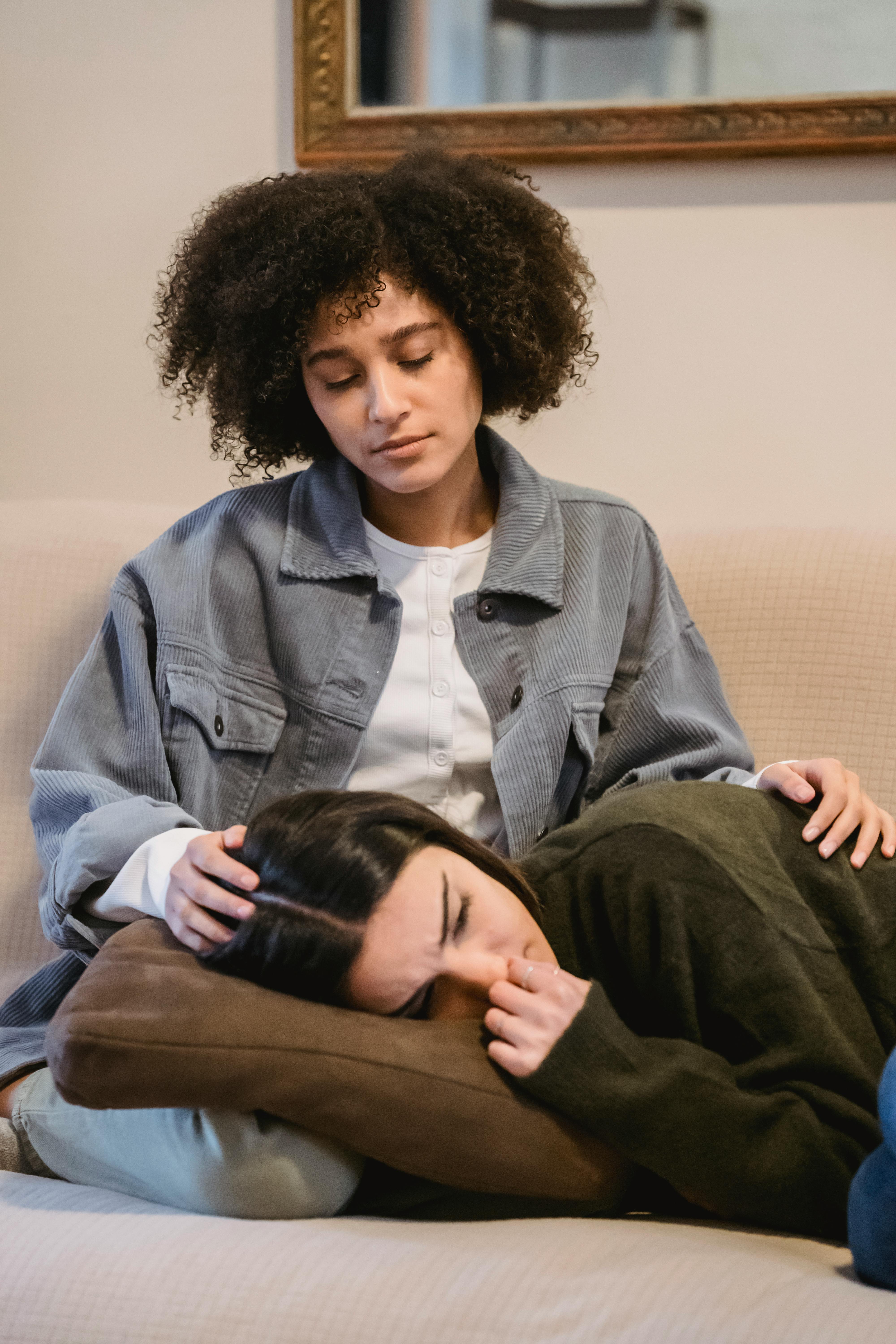 ethnic woman lying on knees of black female friend and crying