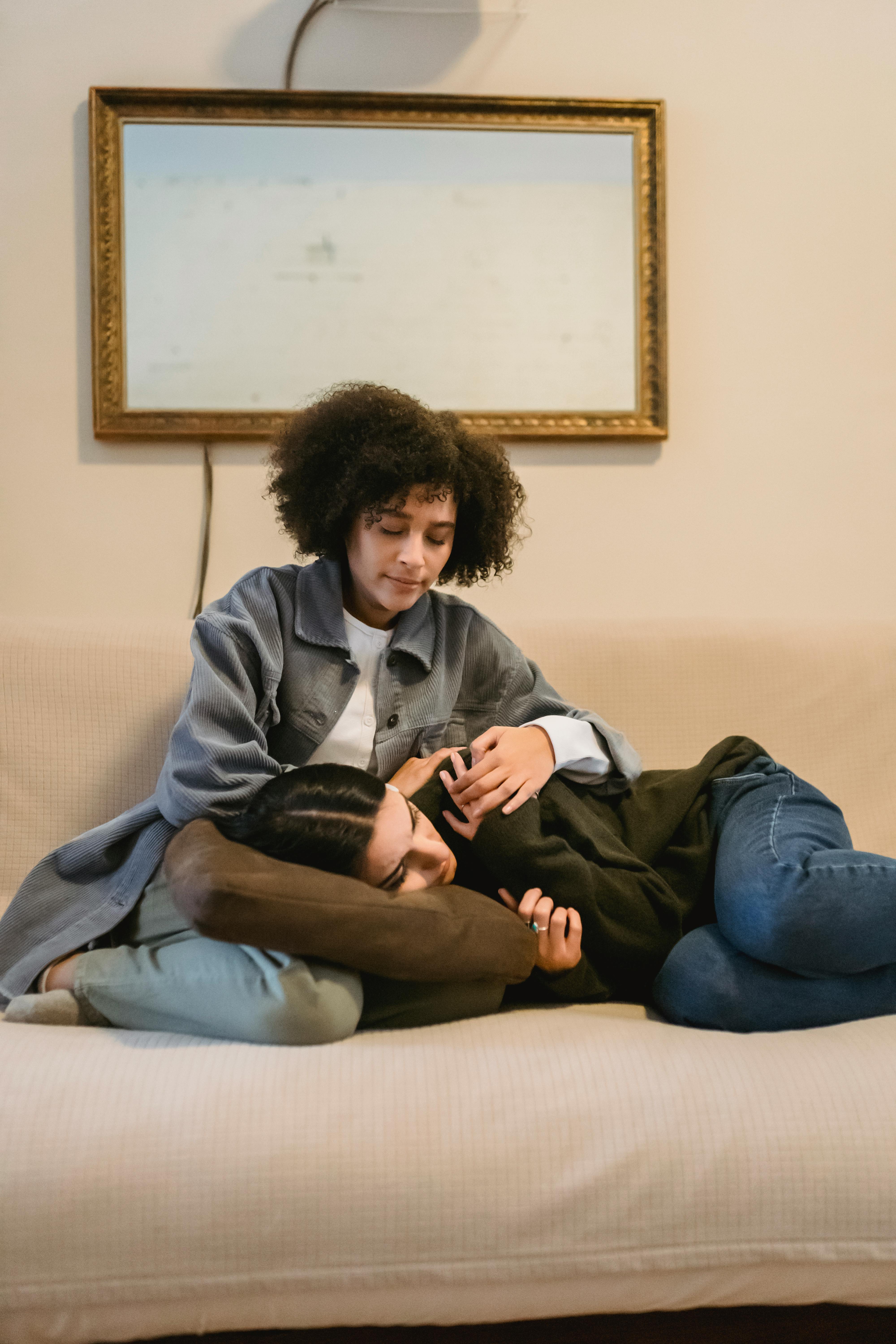 thoughtful young black lady calming upset female friend on couch