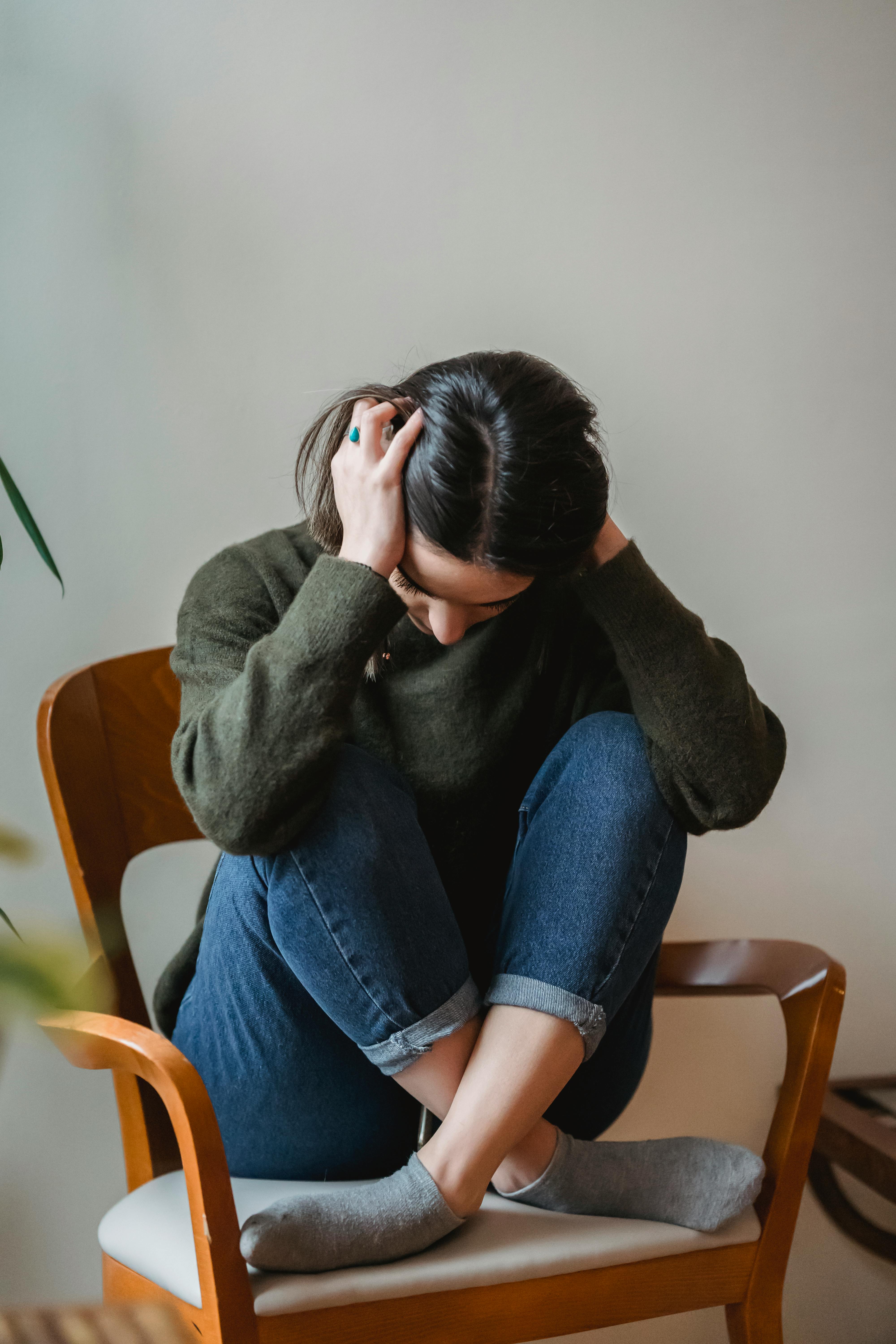 anxious young woman cover wing ears with hands sitting on chair