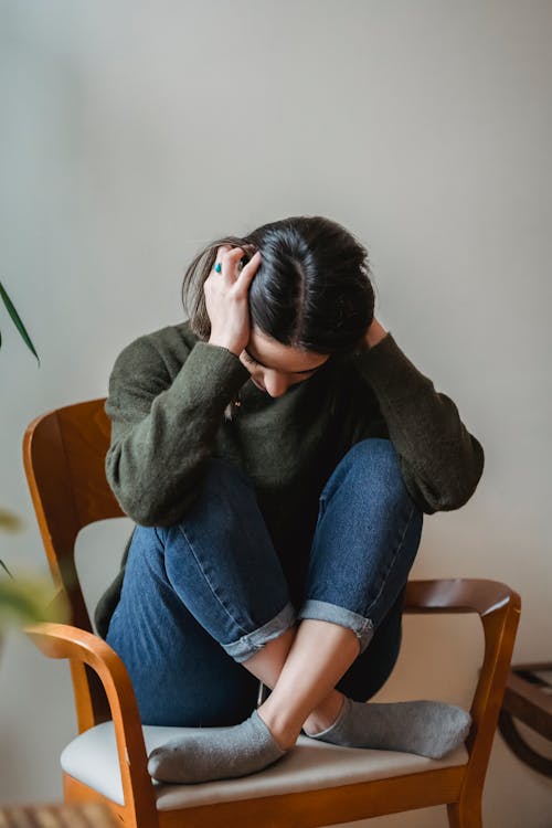 Wanita Dengan Sweater Abu Abu Dan Jeans Denim Biru Duduk Di Kursi Kayu Coklat