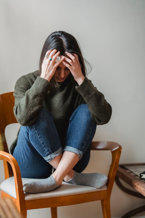 Vrouw In Grijze Trui En Blauwe Denimjeans Zittend Op Bruine Houten Stoel