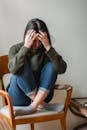 Stressed young ethnic woman grabbing head while sitting on chair