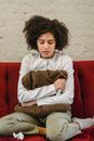 Full body of sorrowful young African American female millennial with curly hair embracing pillow and crying while sitting on sofa at home