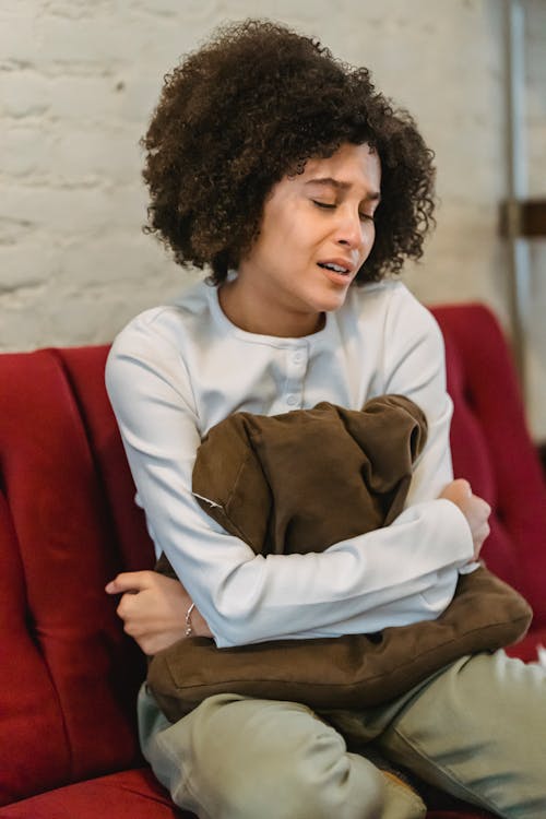 Free Depressed African American female in casual wear with closed eyes crying while sitting on comfortable sofa in living room at home Stock Photo